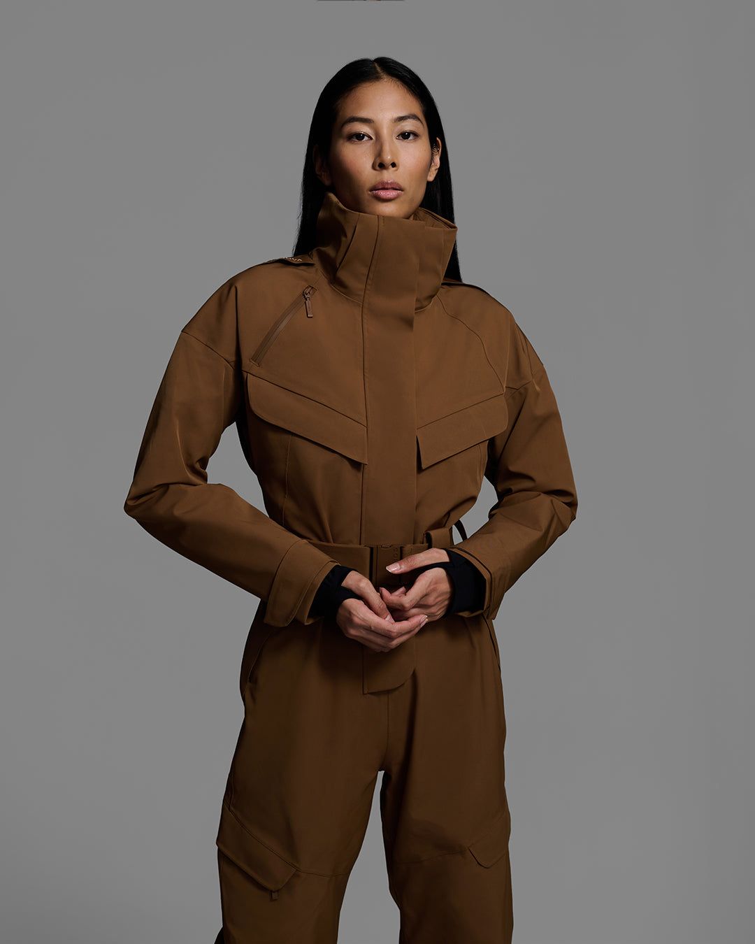 Front detail view of a female model wearing a belted sepia brown color ski suit made of technical waterproof fabric and zippers. #color_sepia