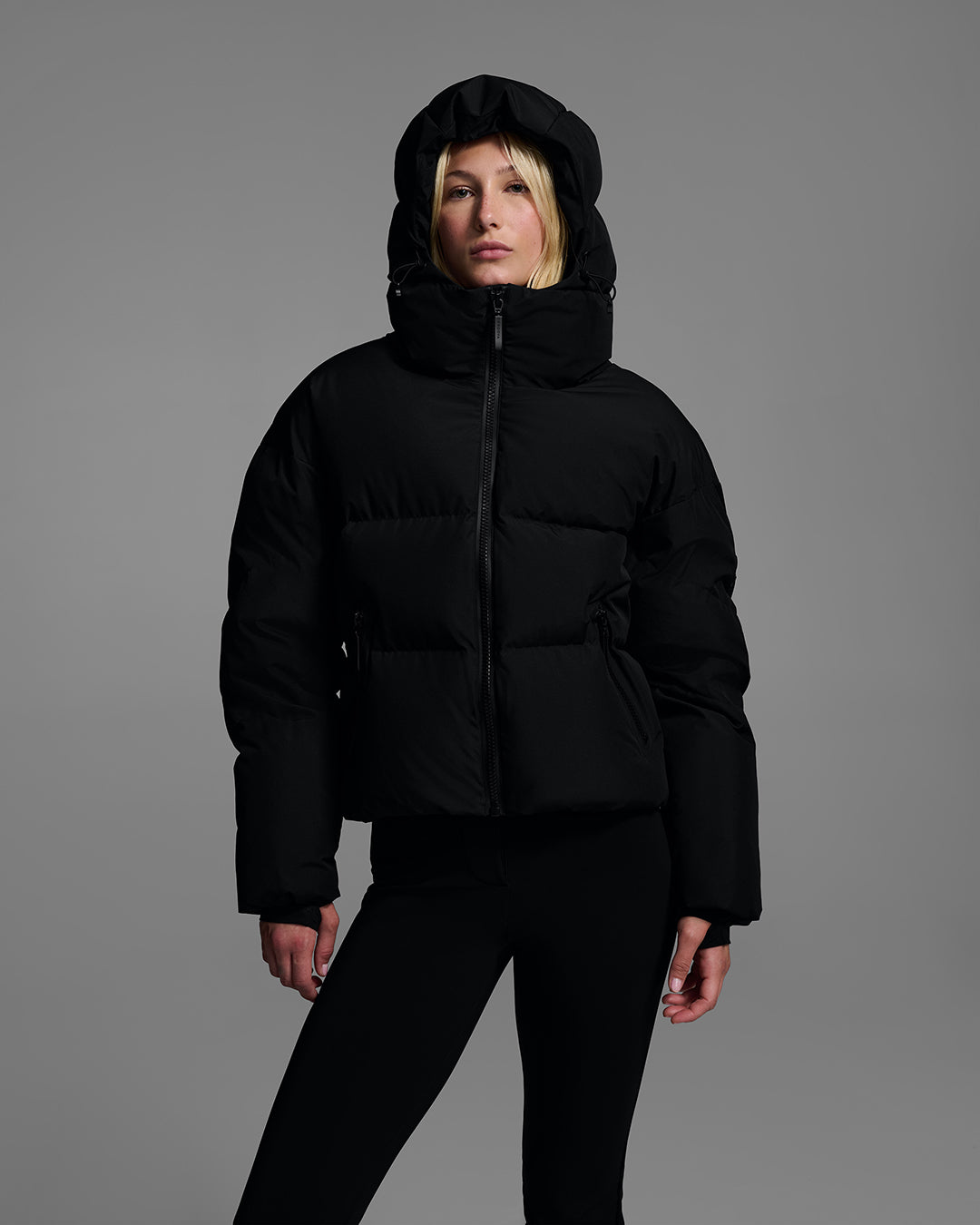 Knee up detail shot of a female model wearing a classic down filled ski jacket in black with a matching ski pant. #color_onyx