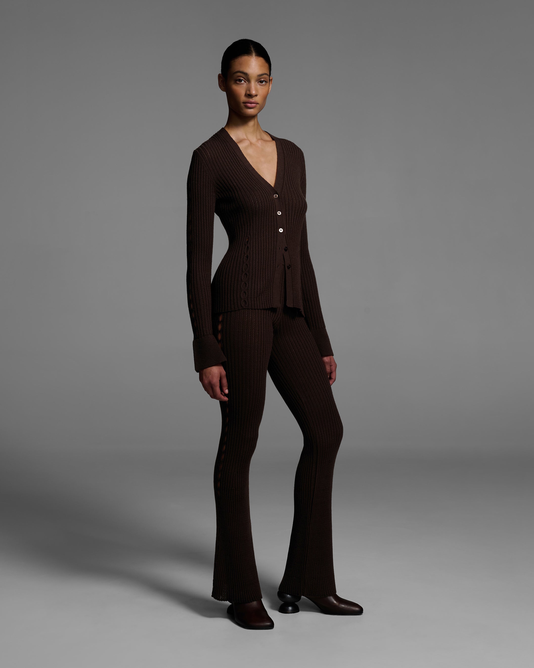 Front view of a woman wearing a chocolate brown knit sweater set with keyholes down the side of arms and legs. #color_chocolate