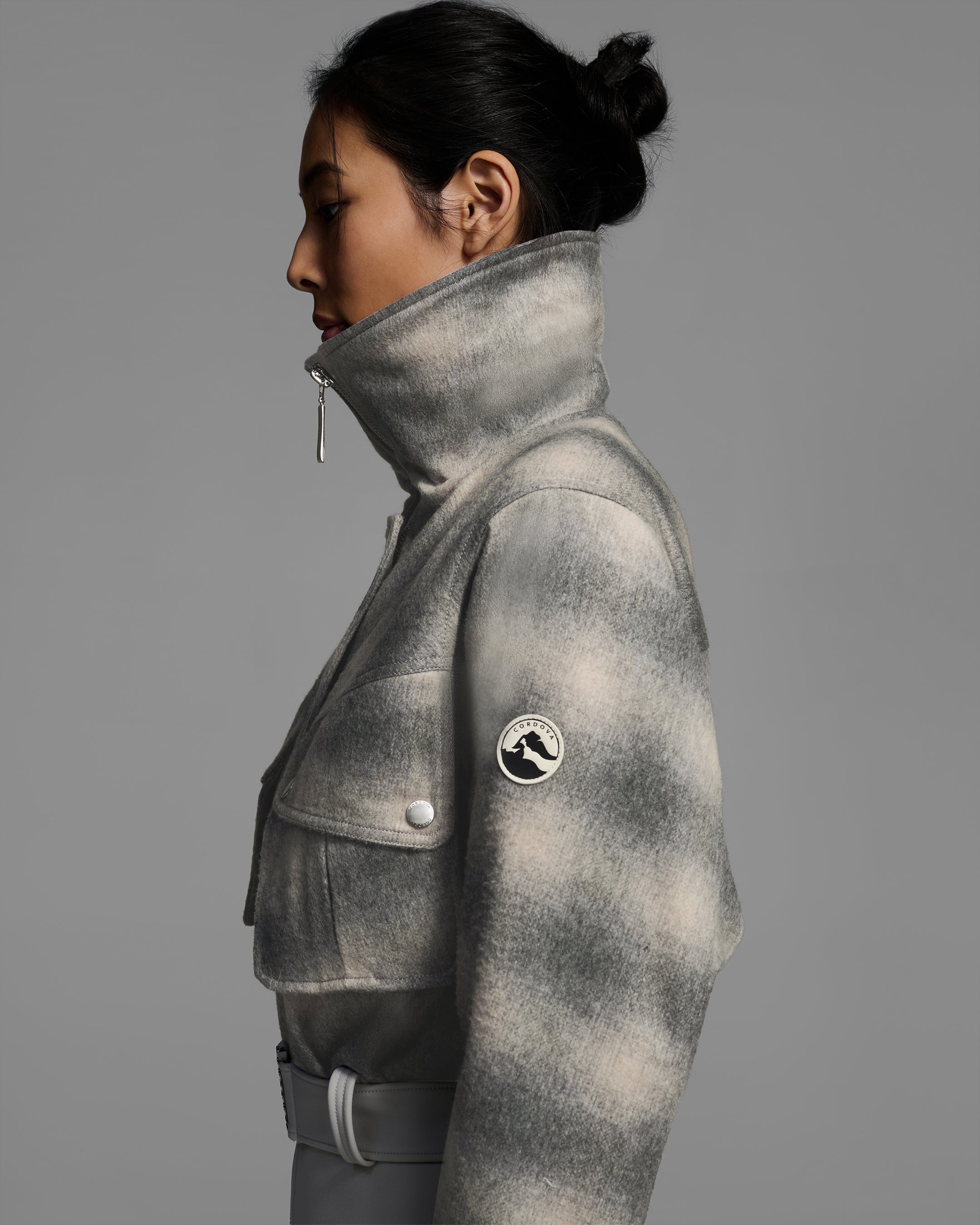 Detail side view of a woman wearing a natural white color and plaid smoke wool top ski suit with belted waist and smoke color 4-way stretch bottom. #color_plaid smoke / stone