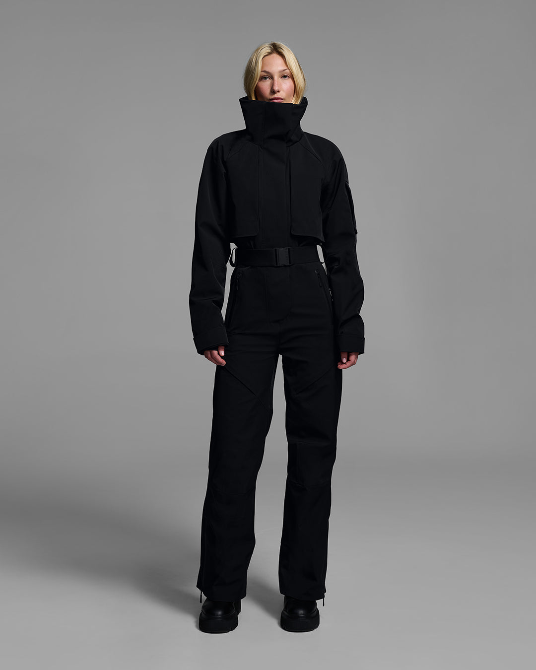 Woman wearing a black color waterproof technical fabric ski suit with a belted waist. #color_onyx