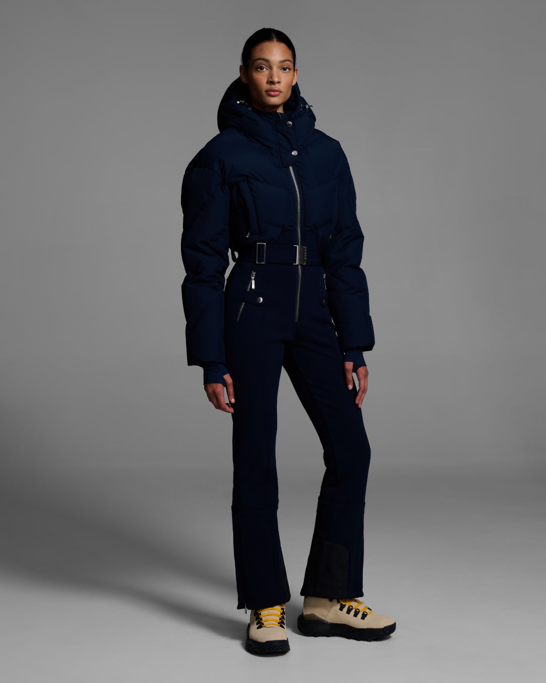 Female model wearing a belted indigo blue color ski suit with down filled top and 4-way stretch bottom. #color_indigo