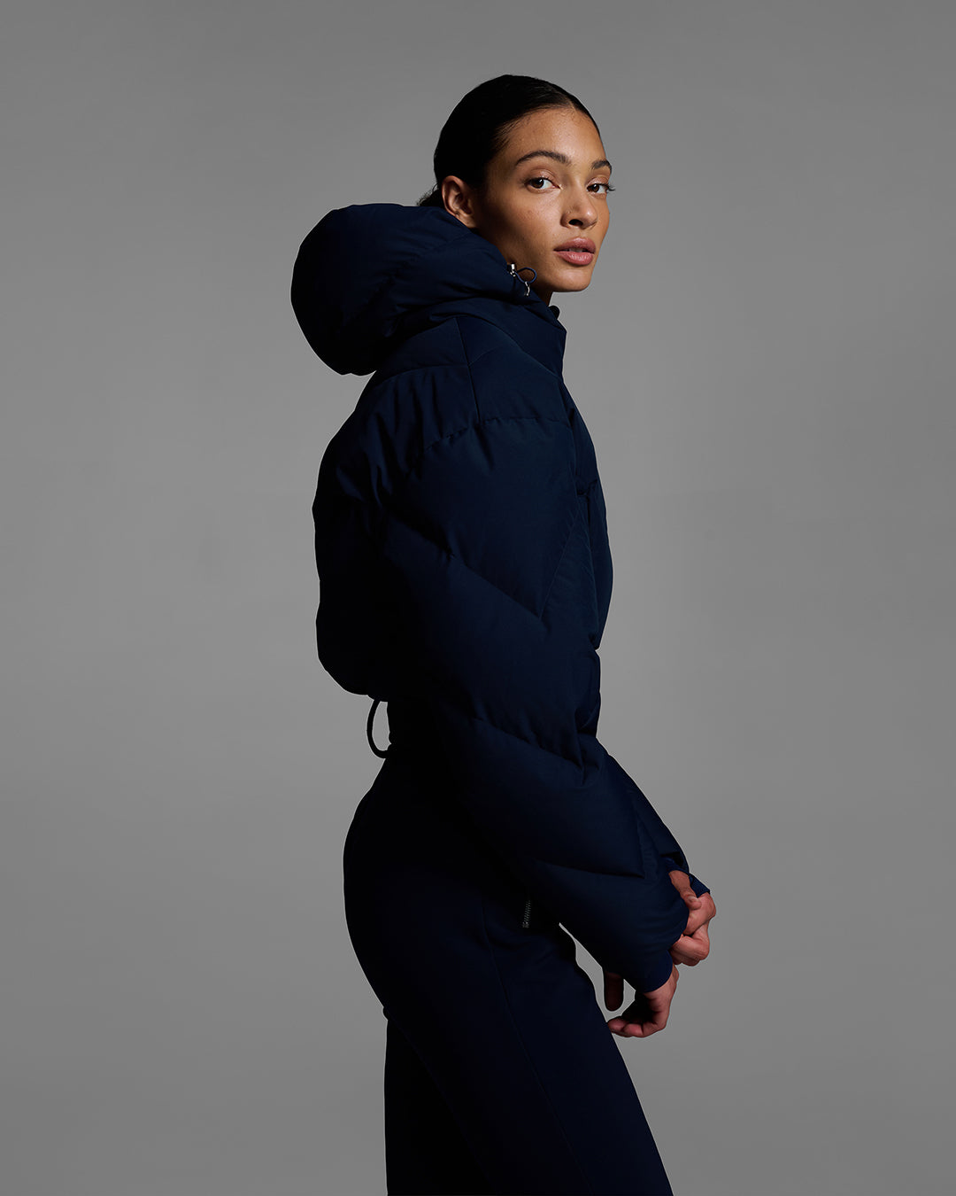 Side view of female model wearing a belted indigo blue color ski suit with down filled top and 4-way stretch bottom. #color_indigo