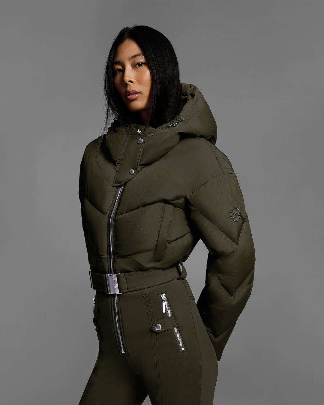 Detail view of a female model wearing a belted khaki green color ski suit with down filled top and 4-way stretch bottom. #color_khaki