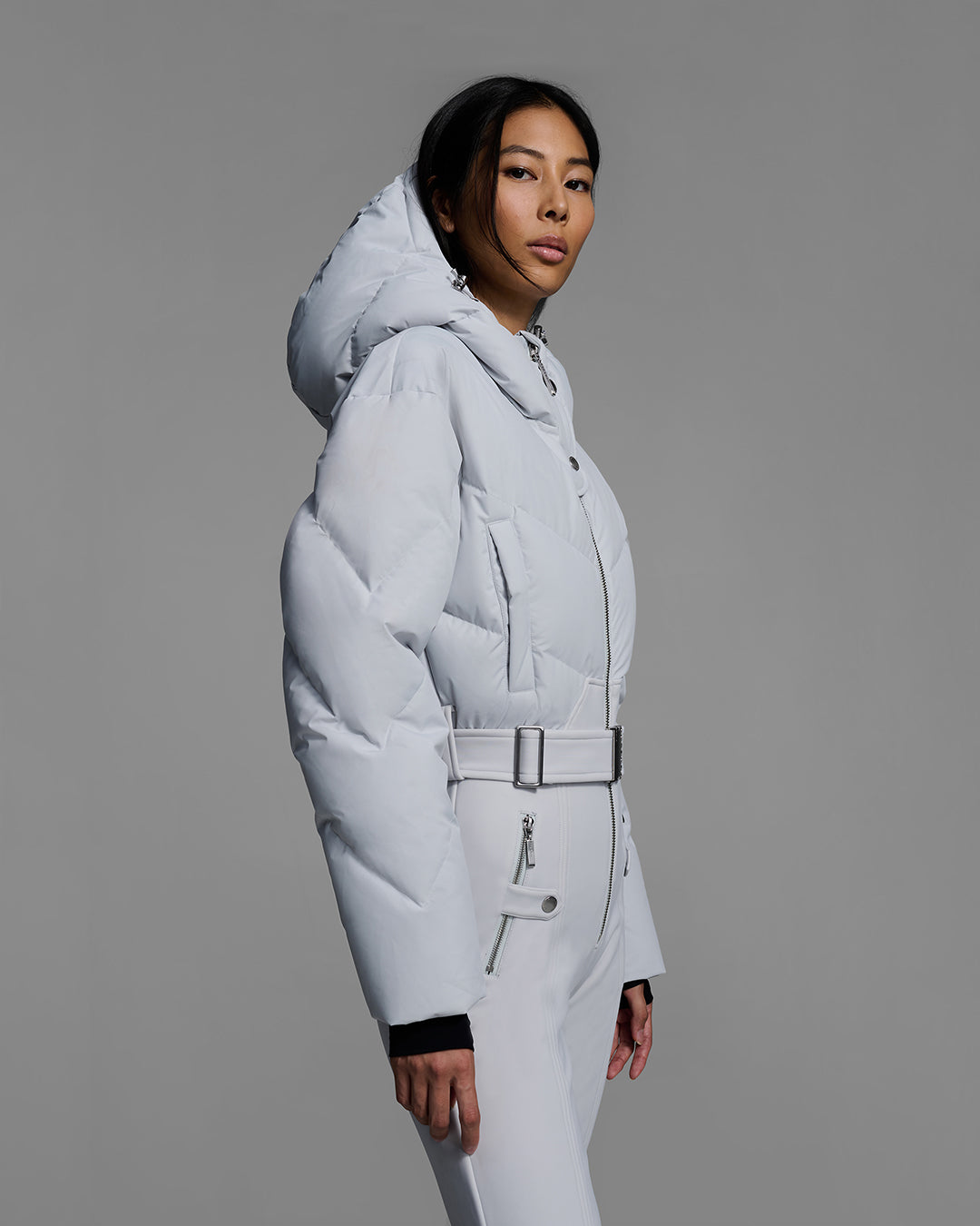 Detail shot of a female model wearing a belted smoke gray color ski suit with down filled top and 4-way stretch bottom. #color_smoke