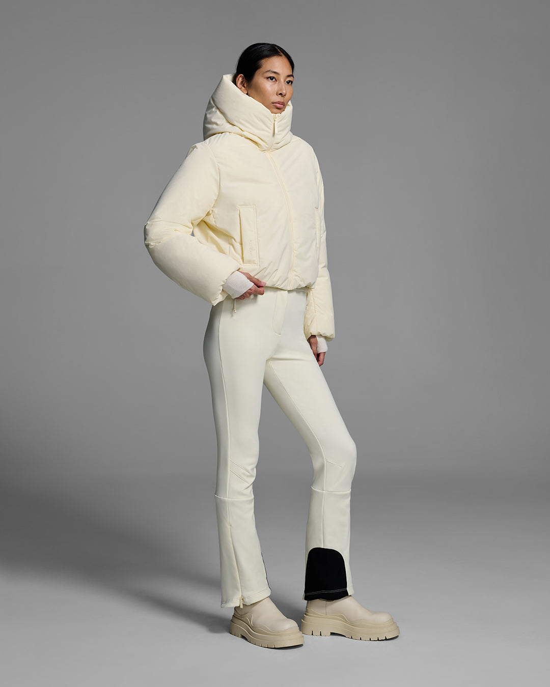 Female model wearing a down filled ski jacket in alabaster off-white fabric, zipped up with a matching off-white ski pant. #color_alabaster