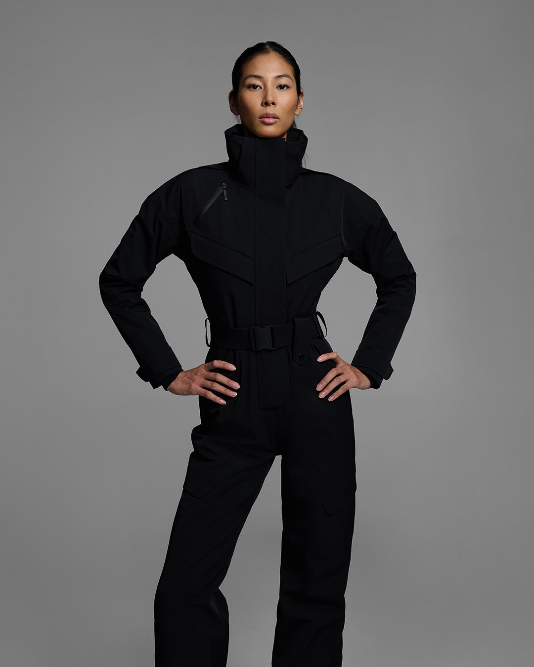 Close up view of a female model wearing a belted onyx black color ski suit made of technical waterproof fabric and zippers. #color_onyx