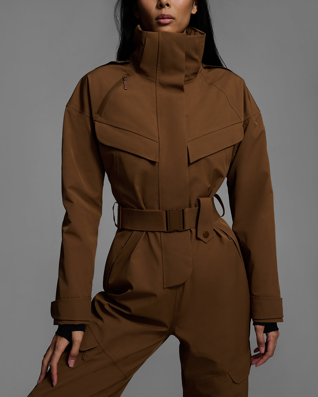 Detail shot of a female model wearing a belted sepia brown color ski suit made of technical waterproof fabric and zippers. #color_sepia