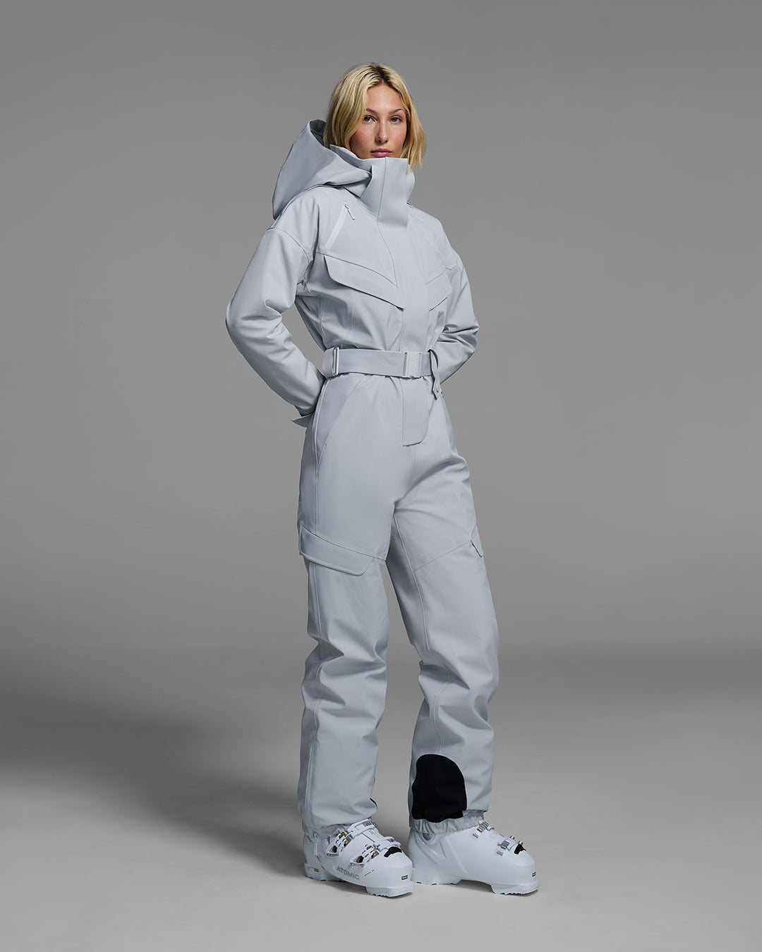 Female model wearing a belted smoke gray color ski suit made of technical waterproof fabric and zippers. #color_smoke