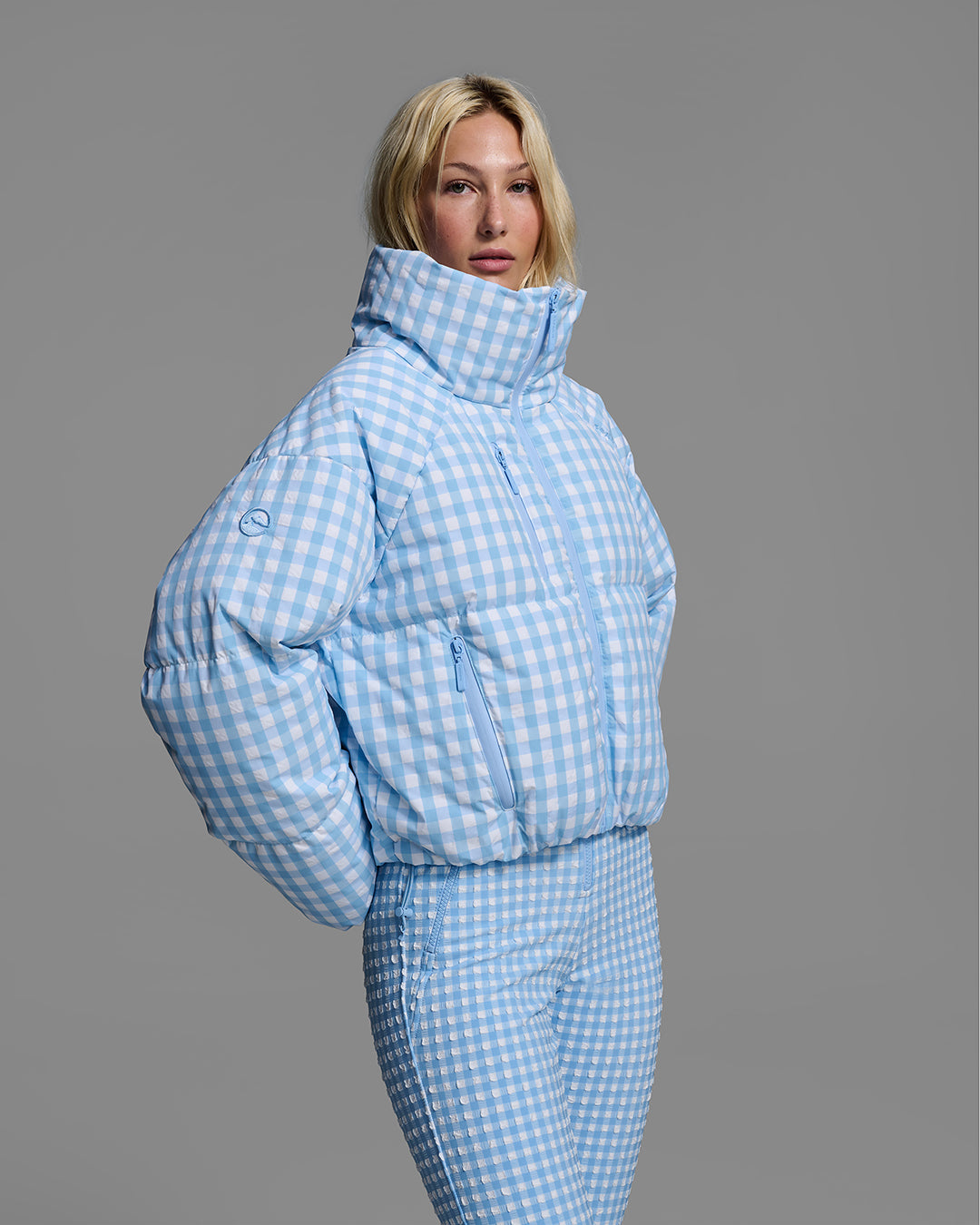 Detail view of a female model wearing a down filled ski jacket in cerulean blue gingham fabric with matching ski suit underneath. #color_cerulean gingham