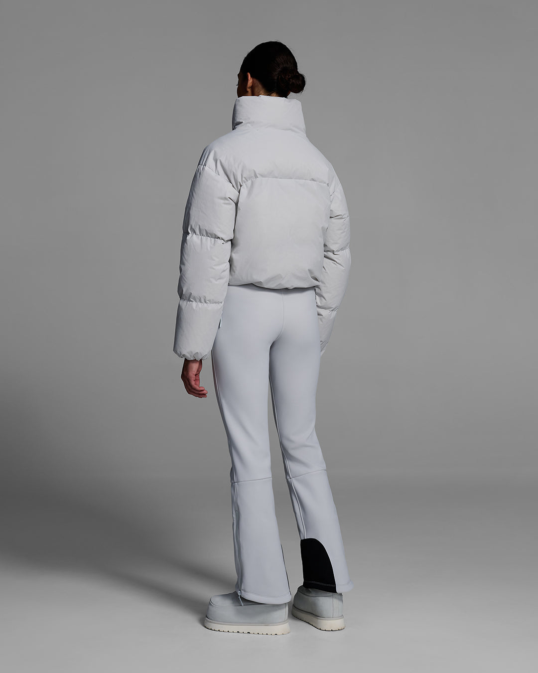 Back view of a female model wearing a down filled ski jacket in smoke gray fabric with a matching ski bib underneath. #color_smoke