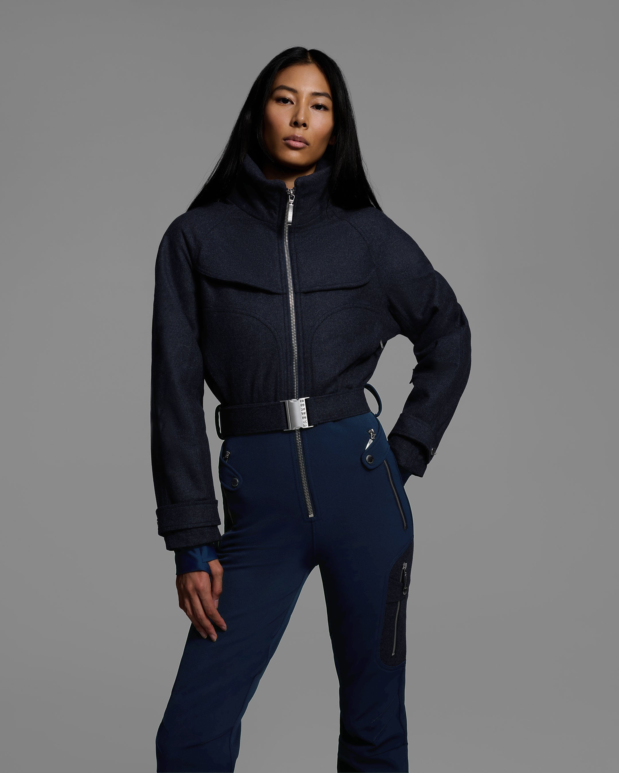 Detail view of a female model wearing a belted indigo denim melange ski suit with a wool top and 4-way stretch water-resistant fabric bottom. #color_indigo