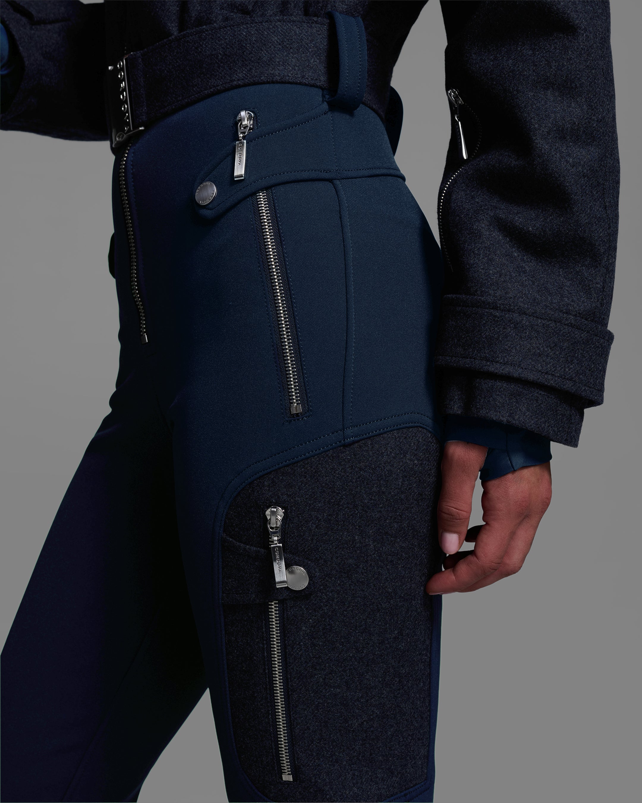 Close up hip detail view of a female model wearing a belted indigo denim melange ski suit with a wool top and 4-way stretch water-resistant fabric bottom. #color_indigo