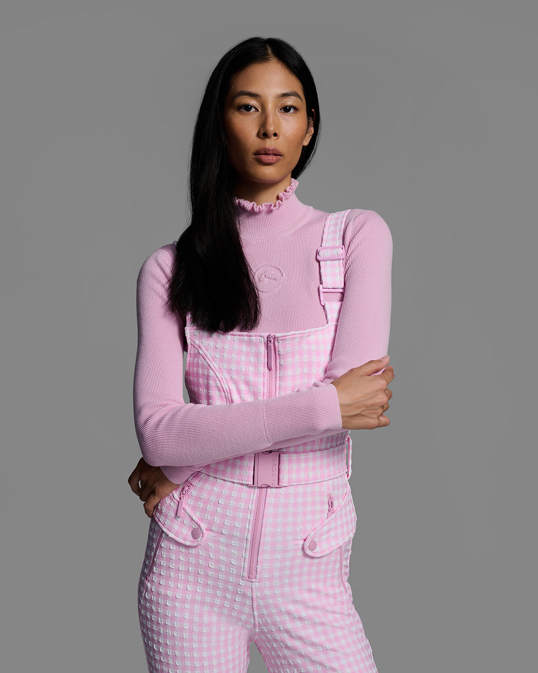 Detail torso view of a female model wearing a belted peony pink color ski bib in a gingham print. #color_peony gingham