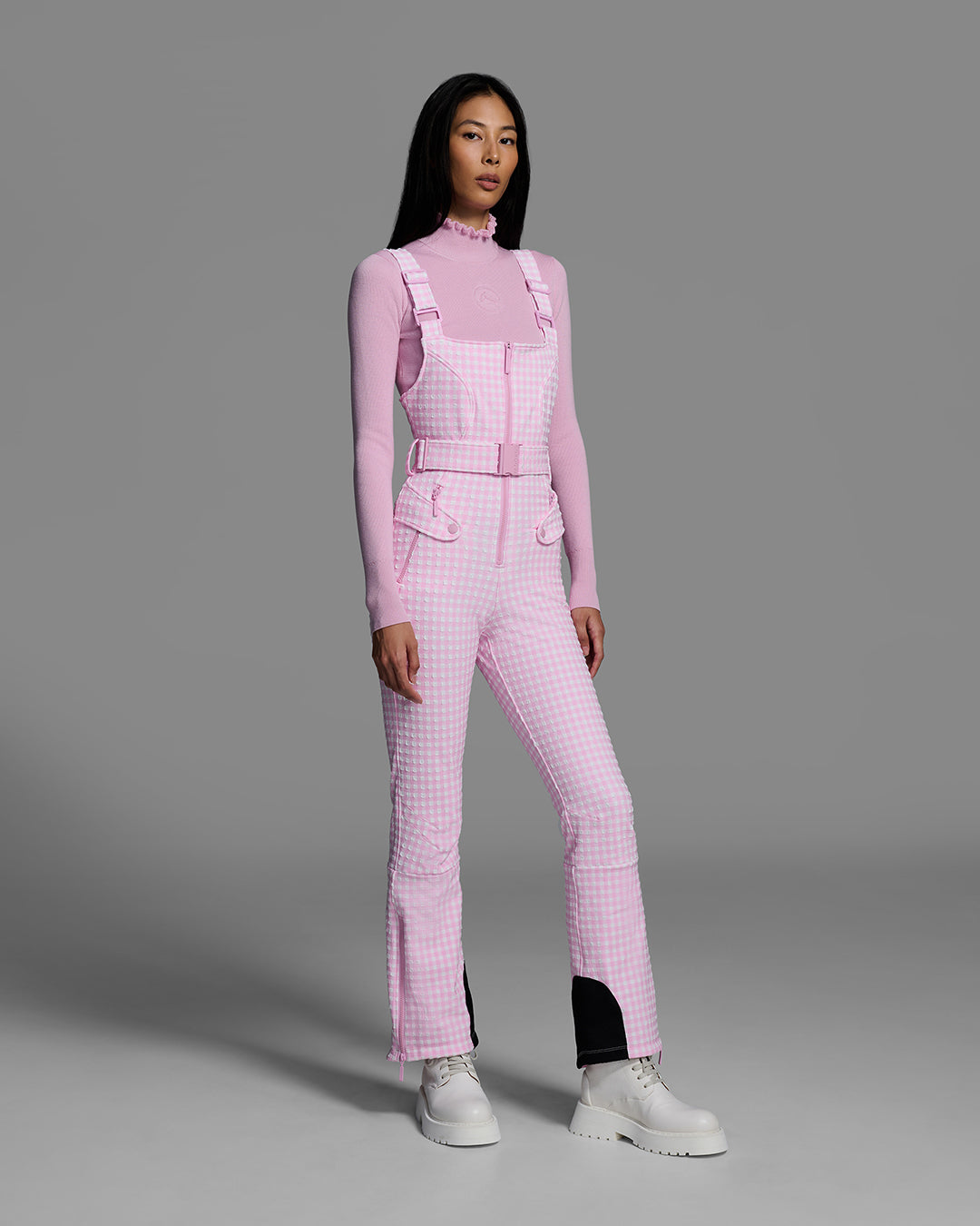 Female model wearing a belted peony pink color ski bib in a gingham print. #color_peony gingham