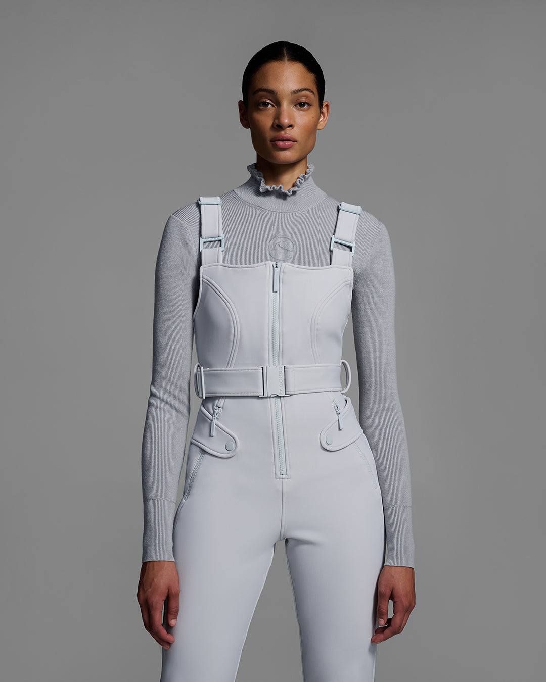 Torso detail view of a female model wearing a belted smoke gray color ski bib with matching gray sweater. #color_smoke