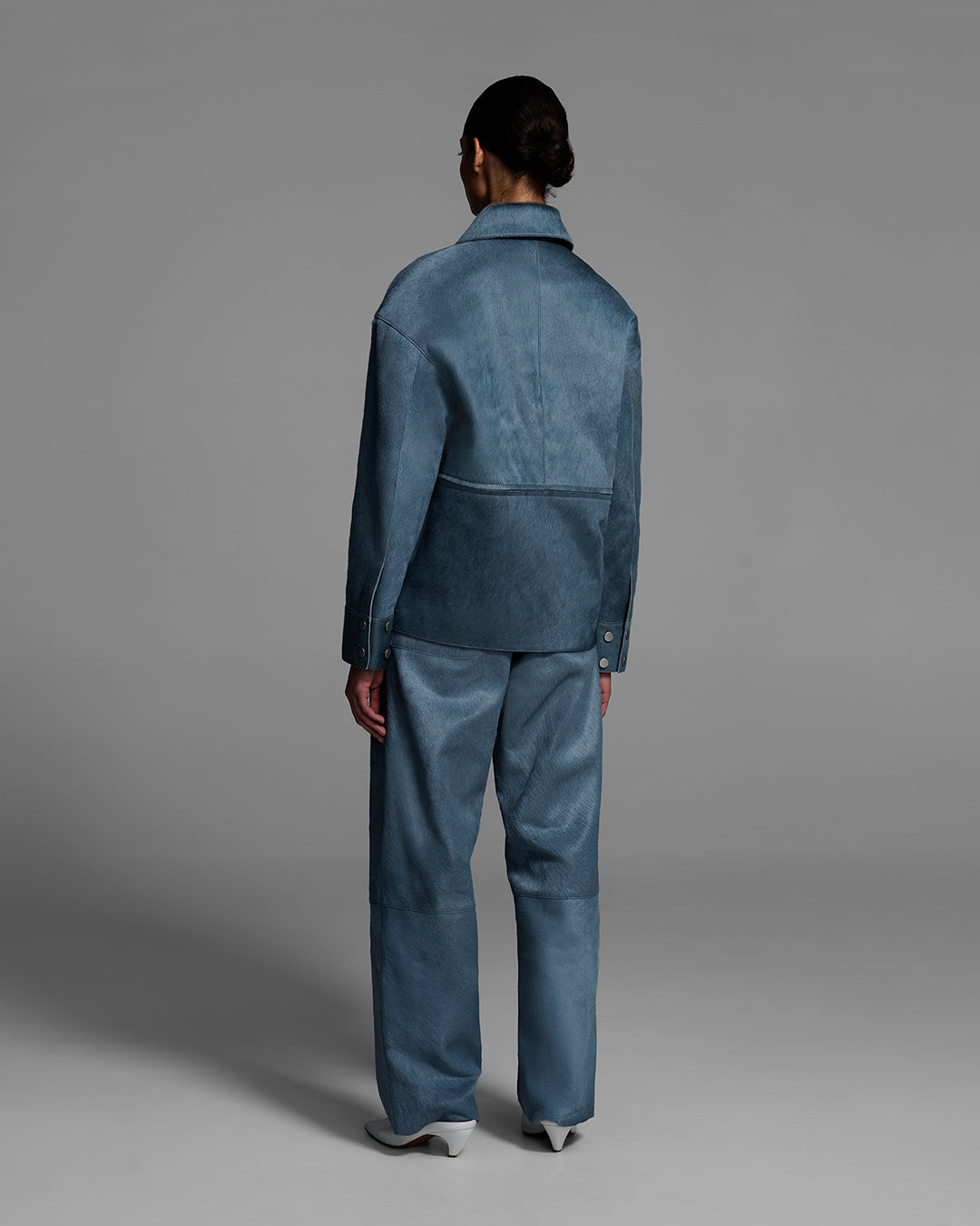 Back view of a female model wearing a hair-on cowhide jacket and pant in storm blue. #color_storm