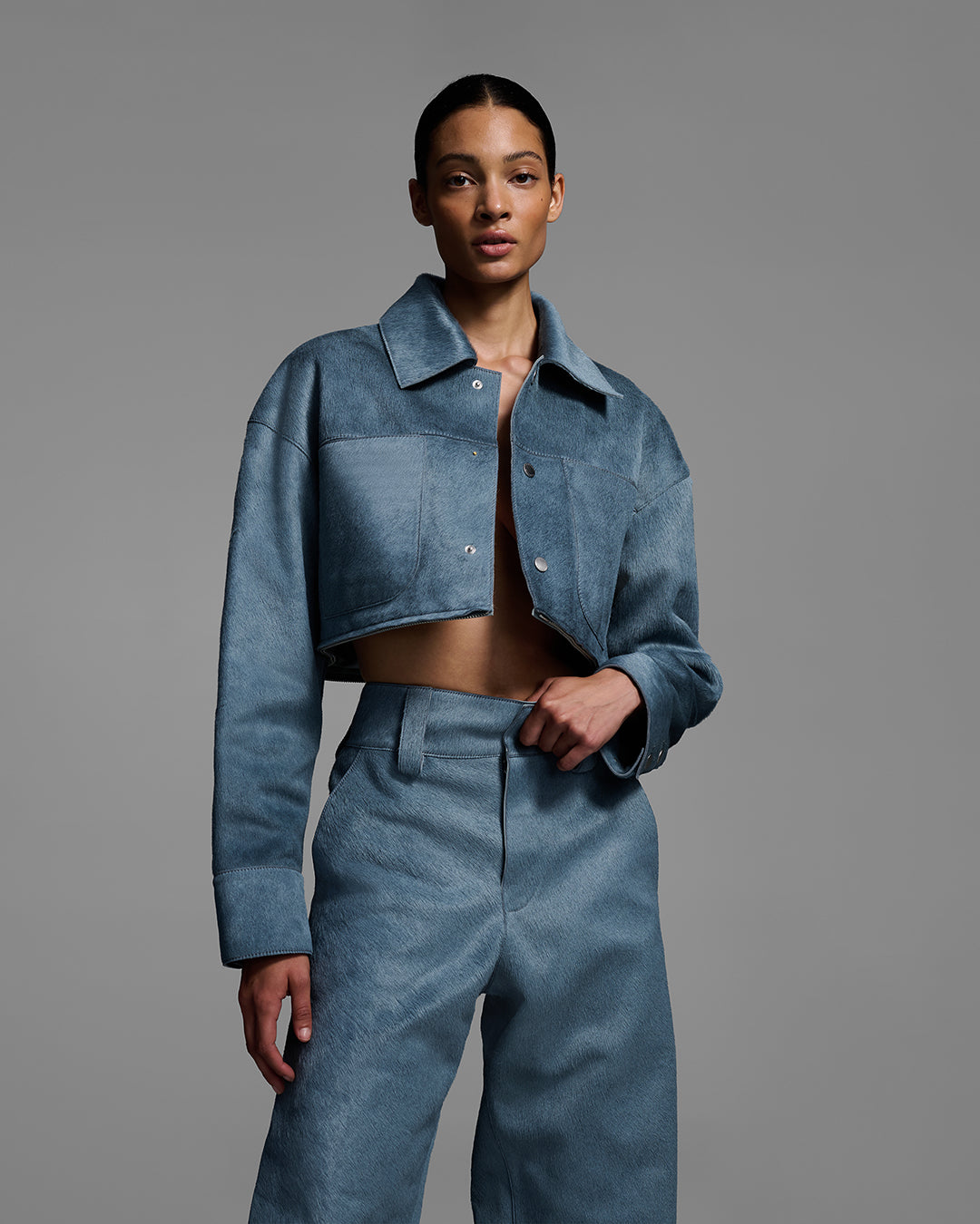 Female model wearing a hair-on cowhide crop jacket, unbuttoned, and a matching pant in storm blue. #color_storm