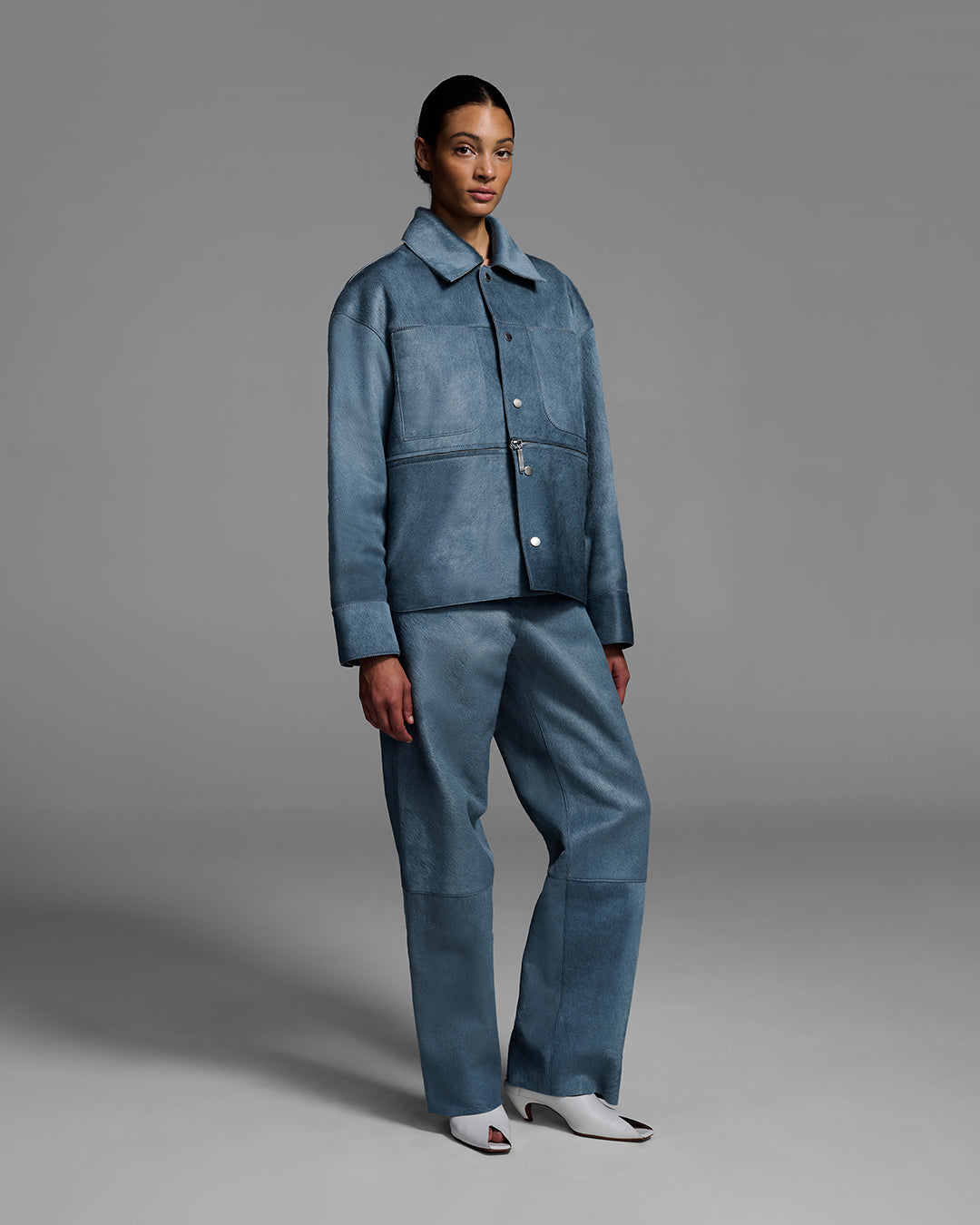 Female model wearing a jacket with a removable panel and matching pant, crafted in hair-on cowhide leather in storm blue color. #color_storm