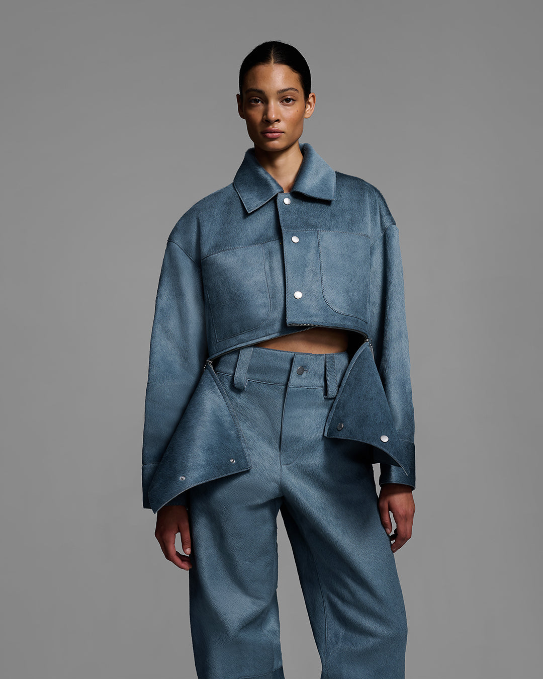 Female model wearing a crop jacket with a removable panel and matching pant, crafted in hair-on cowhide leather in storm blue color. #color_storm