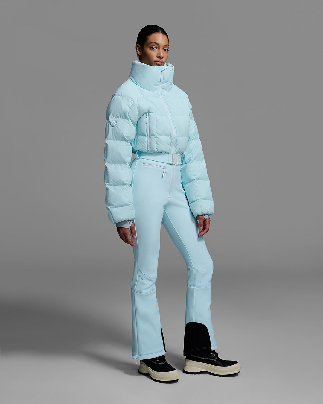 Female model wearing a belted iceberg blue color ski suit with quilted, down filled top and 4-way stretch bottom. #color_iceberg
