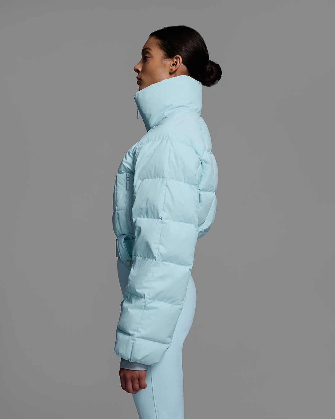 Detail side view of a female model in a iceberg blue ski suit with a quilted down top, belted waist, and 4-way stretch pant. #color_iceberg