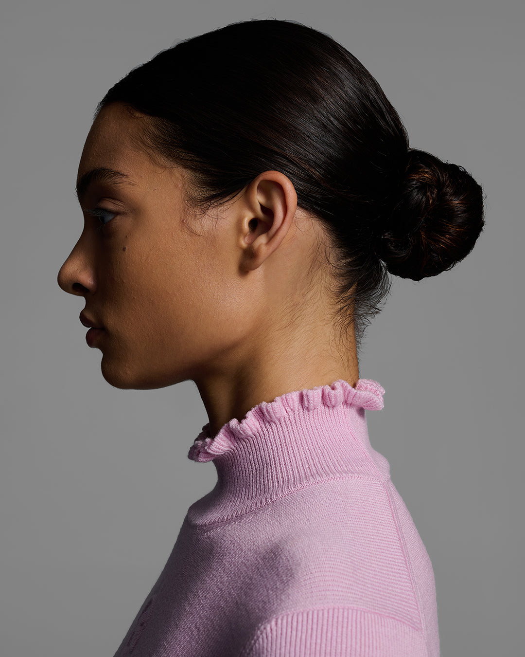 Detail view of the sweater collar of a female model wearing a peony pink knit ski sweater with ruffle edged neck. #color_peony