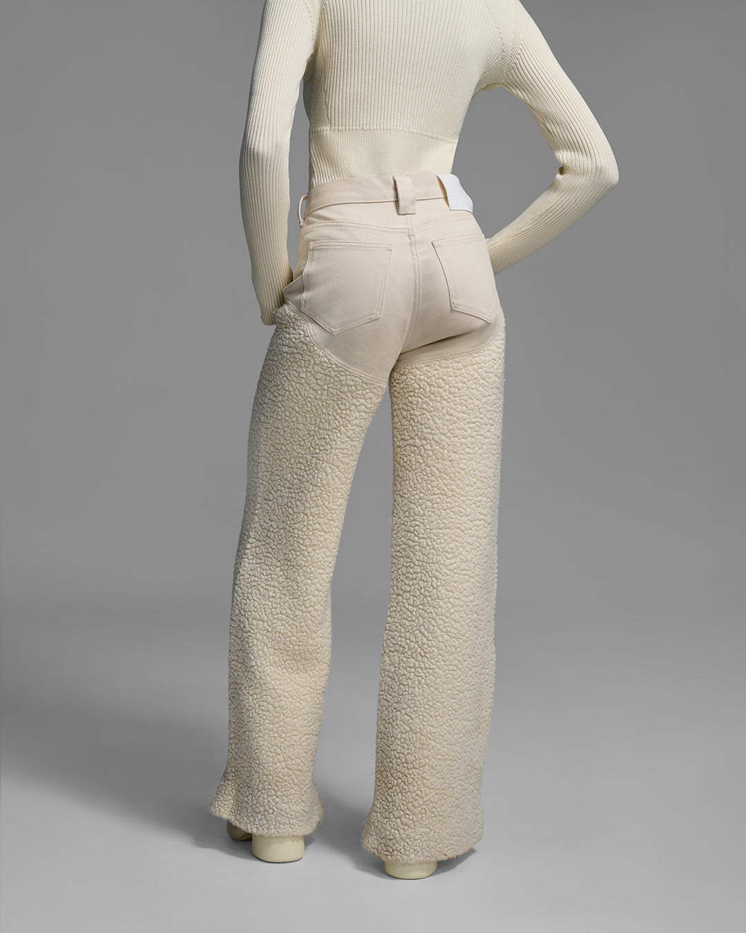 Back view of a female model wearing a resortwear pant with denim bum and sherpa leg in a natural wool fleece color. #color_natural