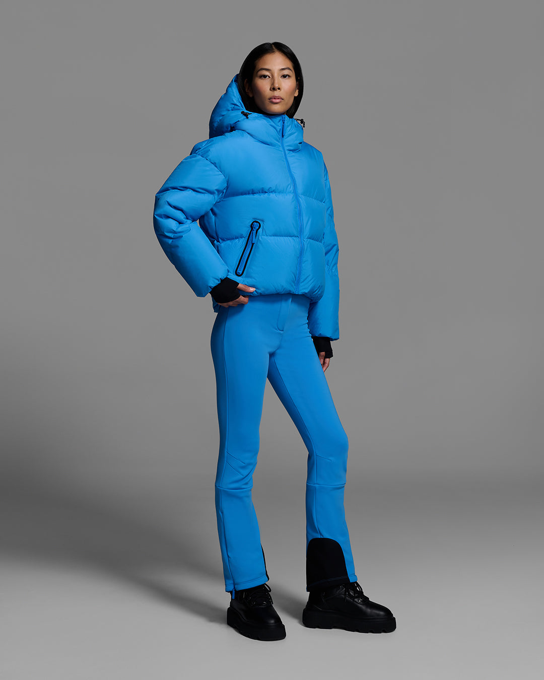 Female model wearing a classic down filled ski jacket in bright blue with a matching ski pant. #color_azul
