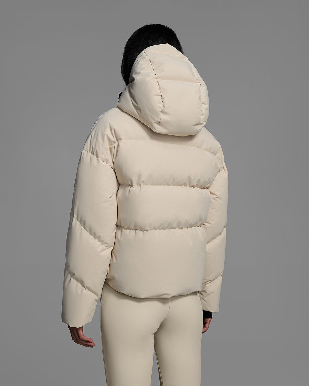 Back view of a knee up detail shot of a female model wearing a classic down filled ski jacket in birch inspired tan with a matching ski pant. #color_birch