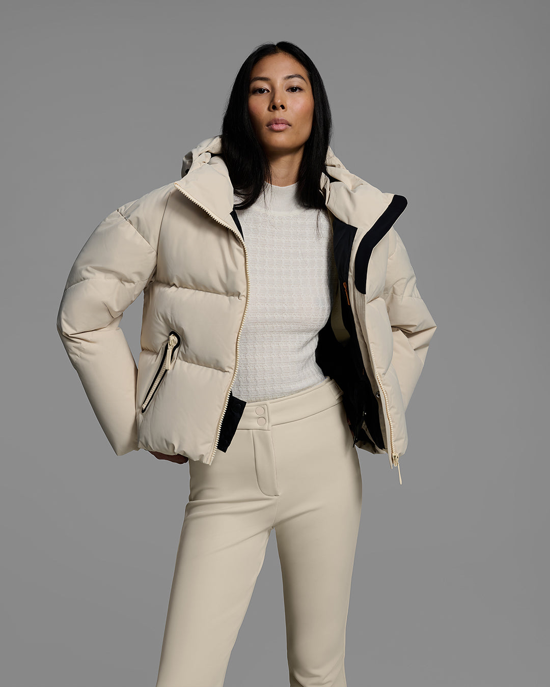 Knee up detail shot of a female model wearing a classic down filled ski jacket, unzipped, in birch inspired tan with a matching ski pant. #color_birch