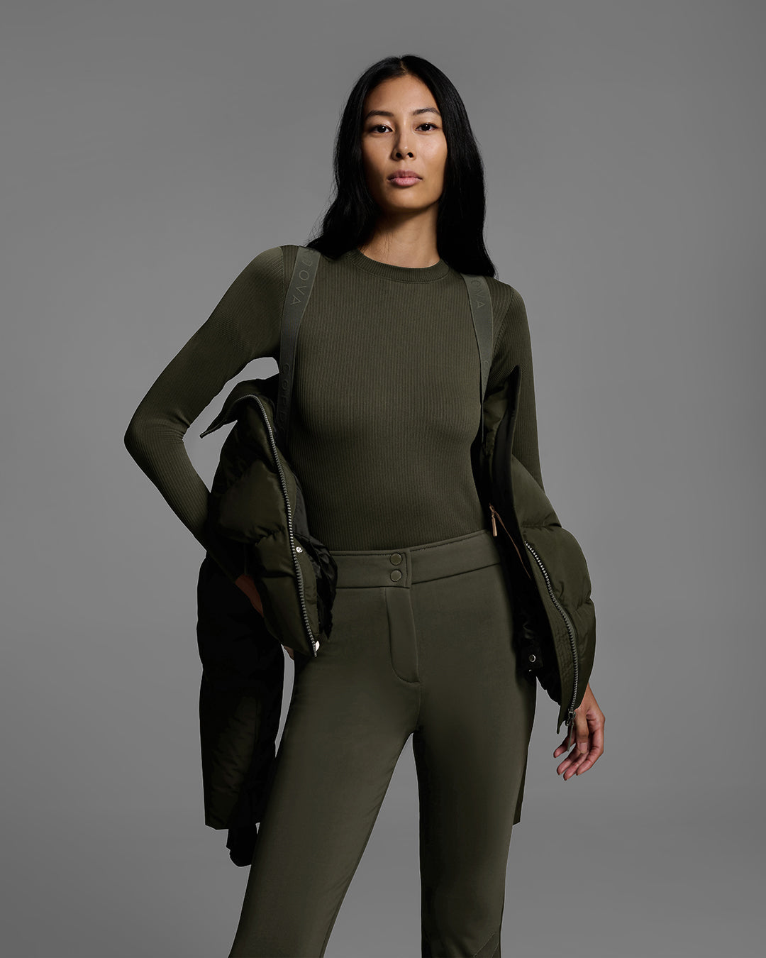 Detail view of female model wearing jacket like a backpack with interior straps. It's a classic down filled ski jacket in khaki green with a matching ski pant. #color_khaki
