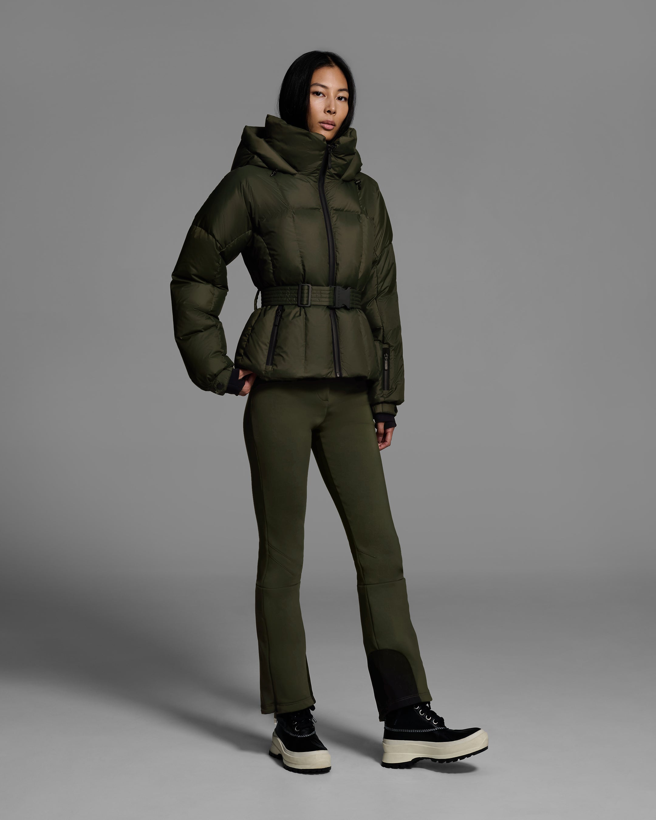 Female model wearing a classic slope style down filled, belted ski jacket in khaki green color with a matching ski pant. #color_khaki
