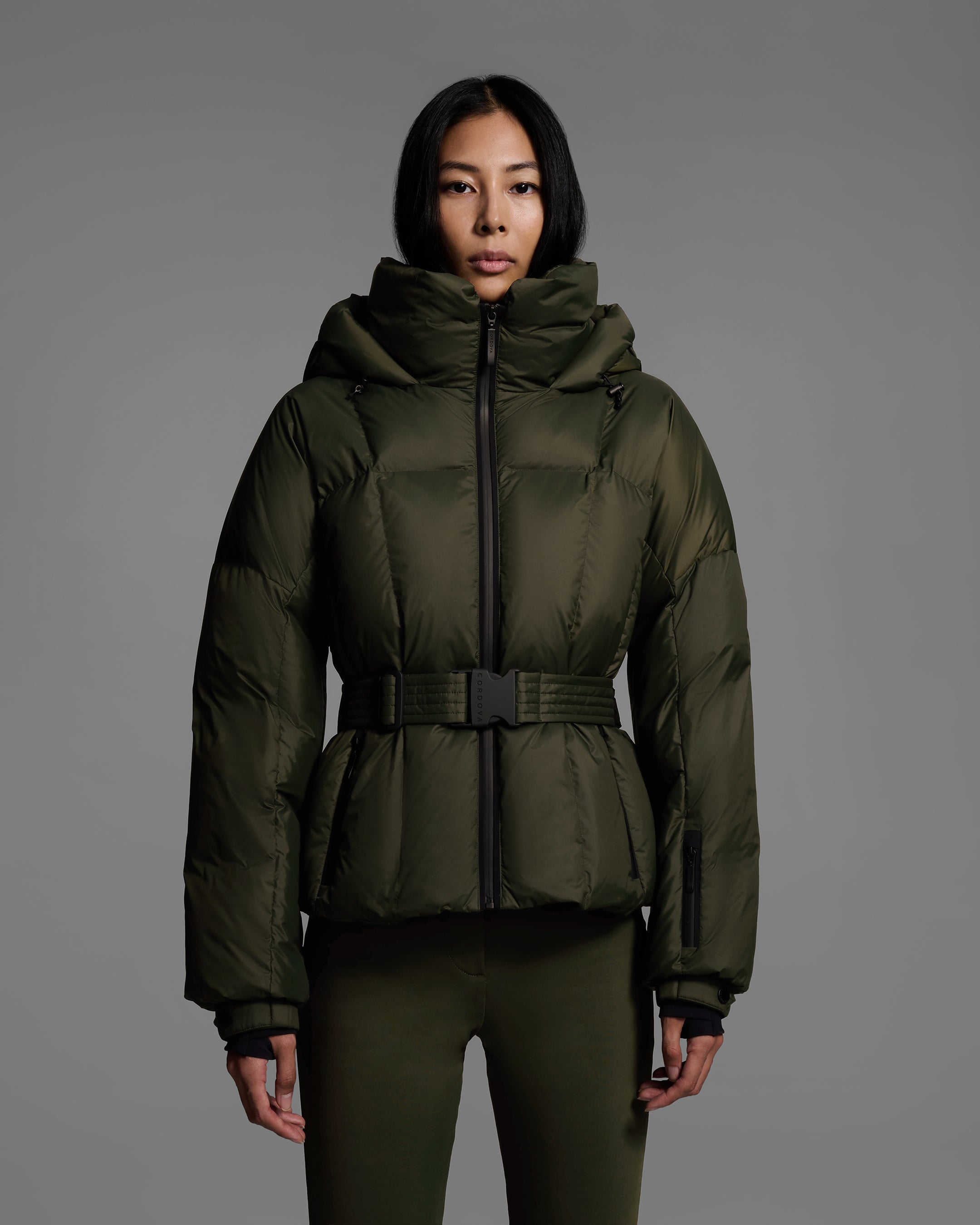 Detail front view of a female model wearing a classic slope style down filled, belted ski jacket in khaki green color with a matching ski pant. #color_khaki