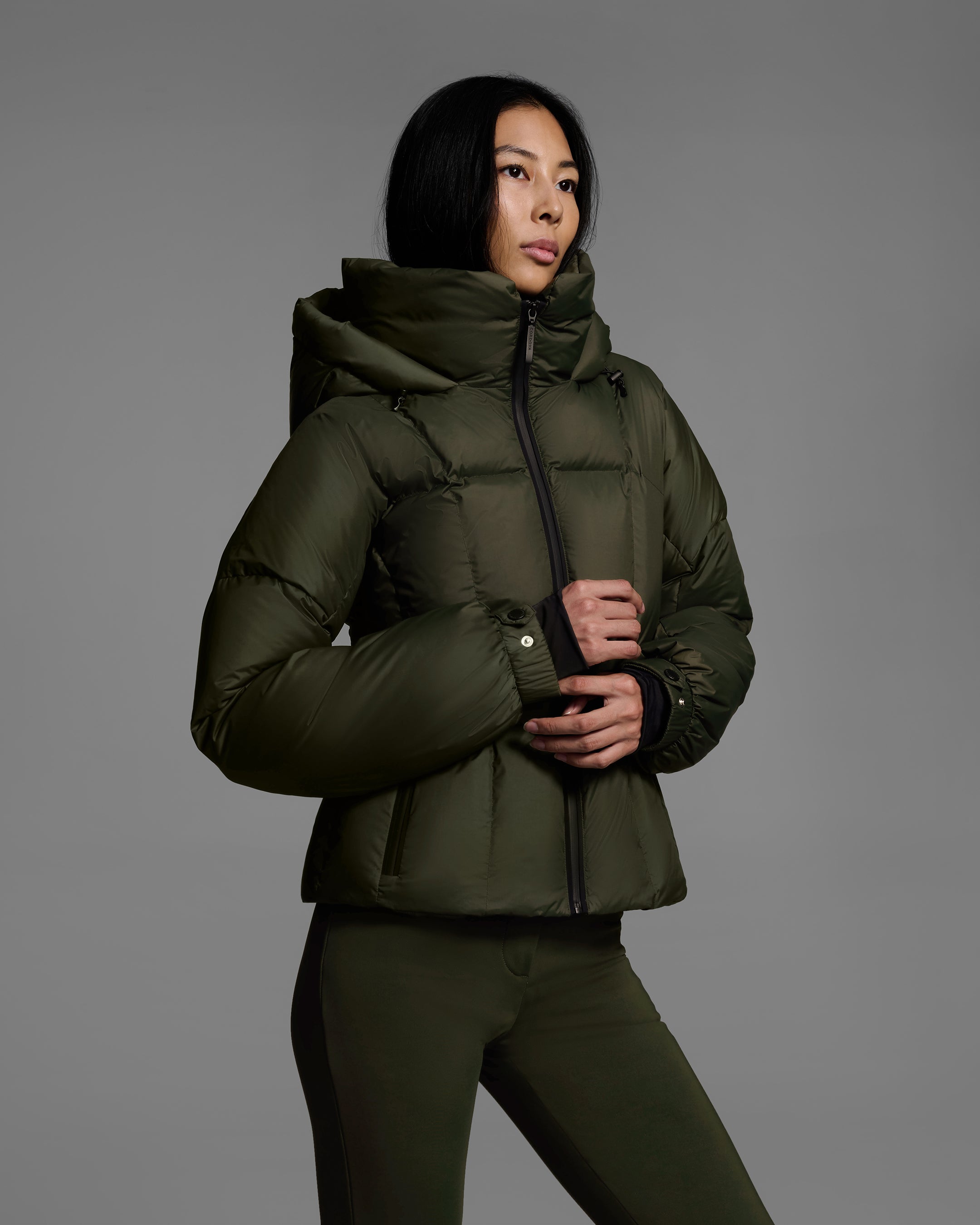 Side detail view of a female model wearing a classic slope style down filled, belted ski jacket in khaki green color with a matching ski pant. #color_khaki