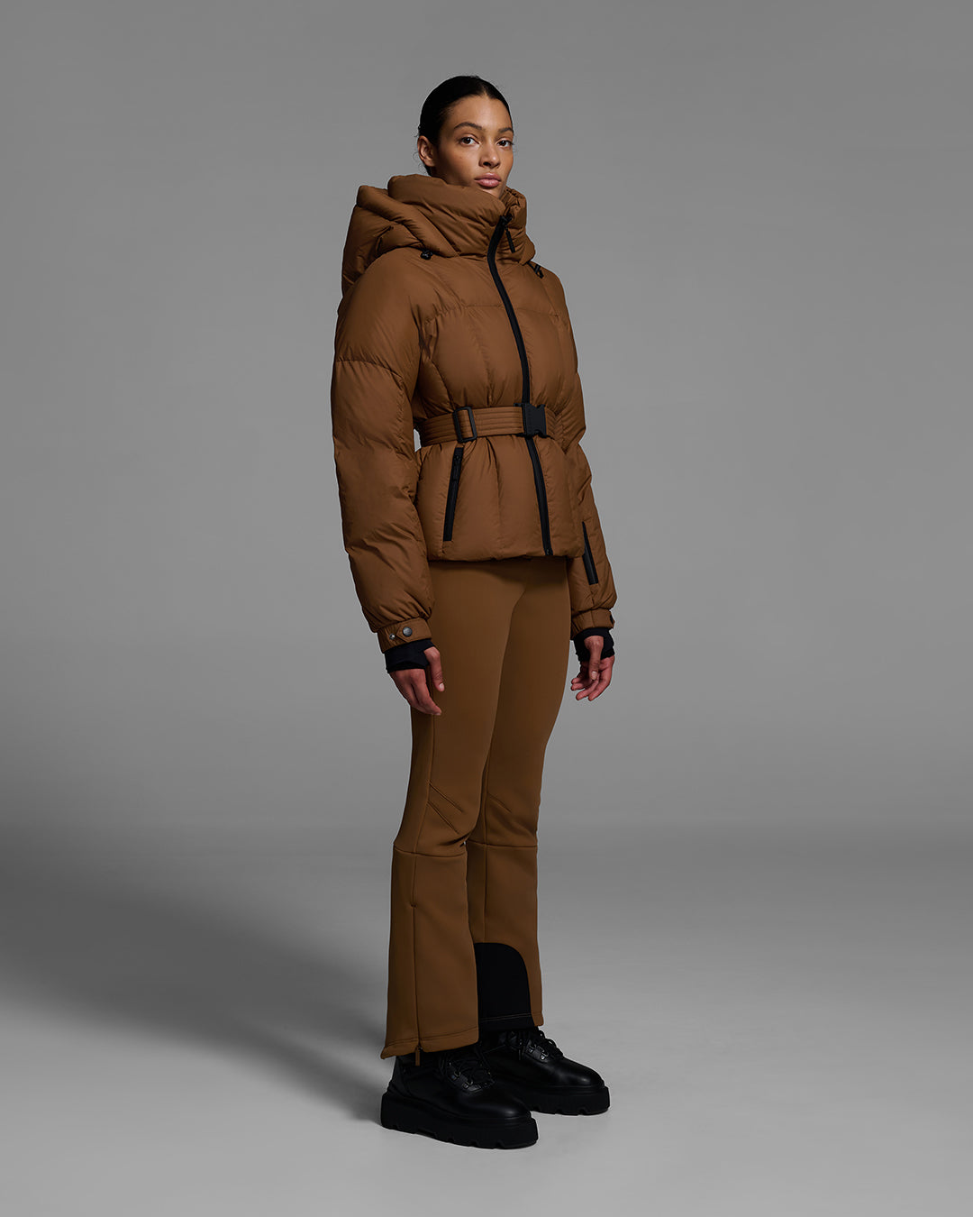 Female model wearing a classic slope style down filled, belted ski jacket in sepia brown color with a matching ski pant. #color_sepia