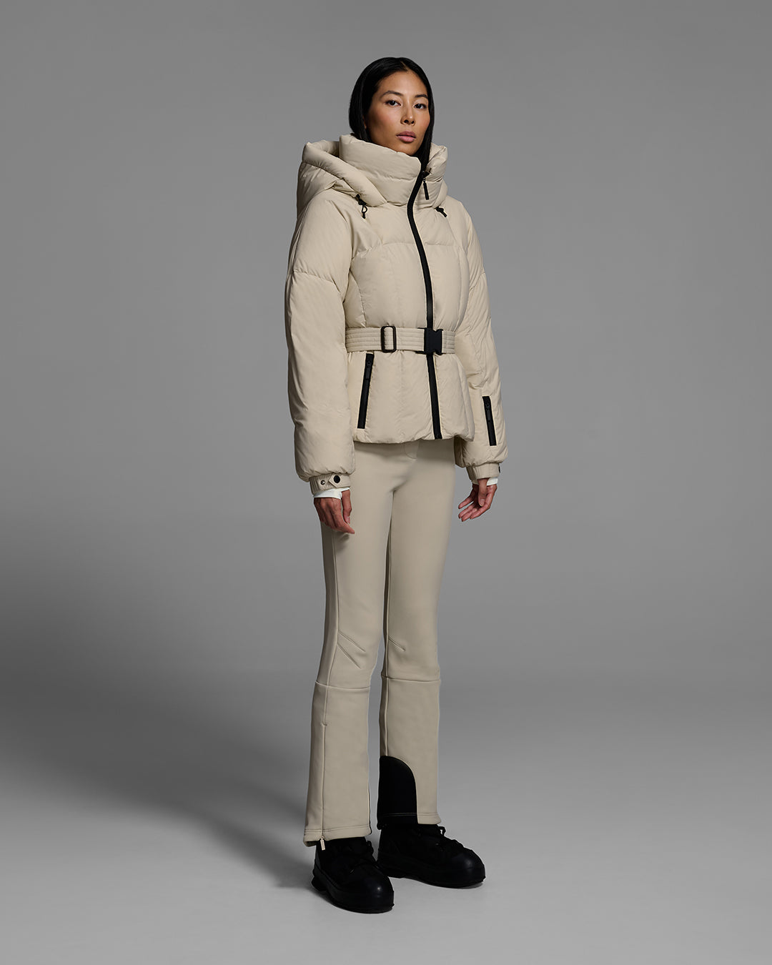 Female model wearing a classic slope style down filled, belted ski jacket in birch inspired tan color with a matching ski pant. #color_birch