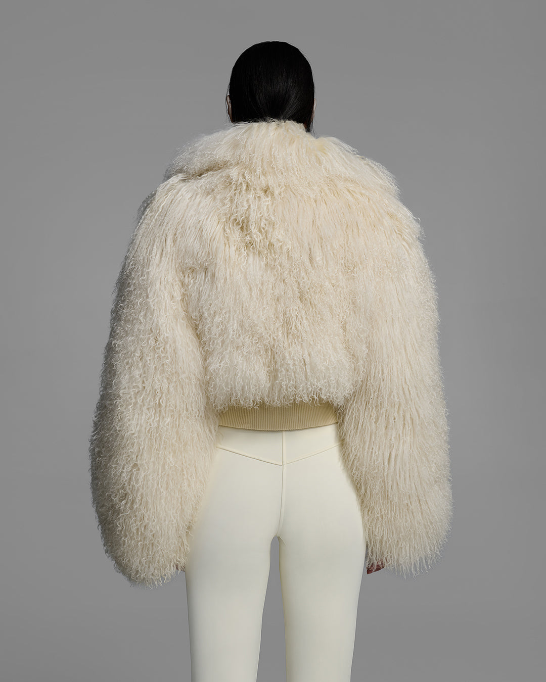 Back view of a female model wearing a natural white color shearling jacket with matching ski pant. #color_alabaster