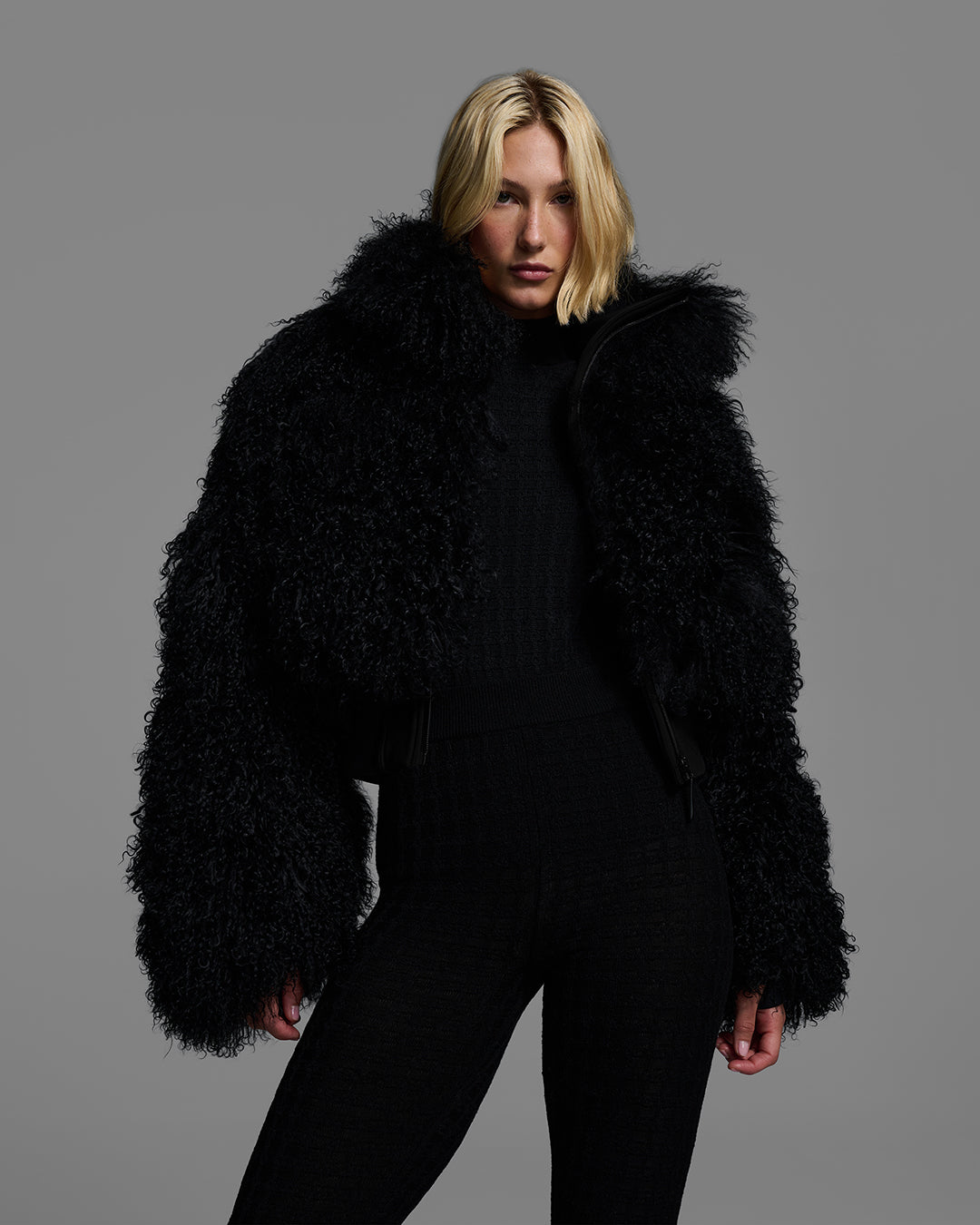 Female model wearing a black color shearling jacket, unzipped, with matching black sweater and ski pant. #color_onyx