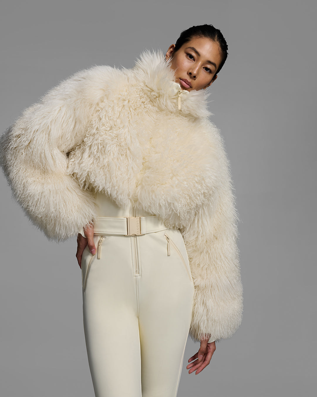 Detail front view of a woman wearing an alabaster white color ski suit with a shearling top, belted waist, and 4-way stretch pant. #color_alabaster