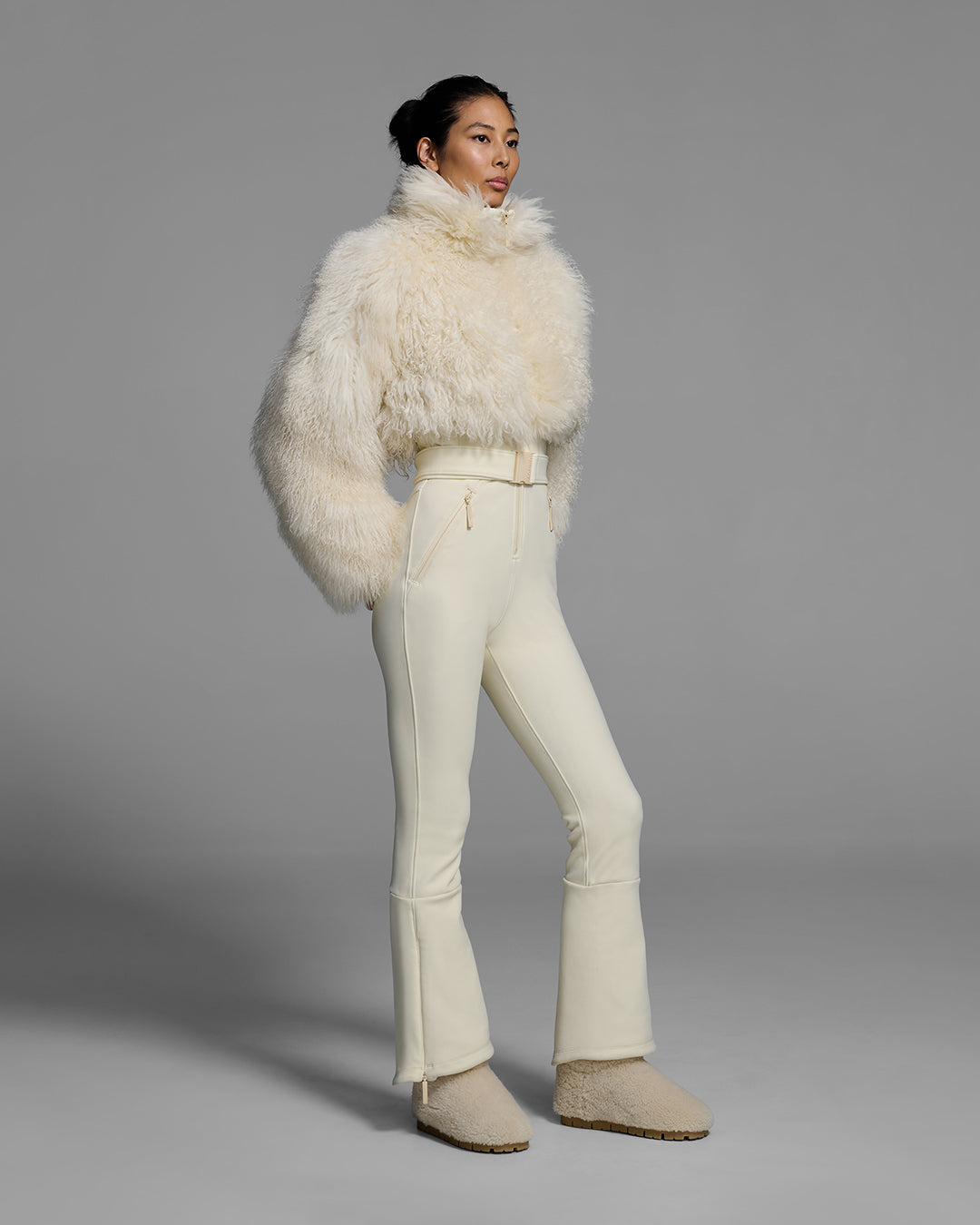 Woman wearing an alabaster white color ski suit with a shearling top, belted waist, and 4-way stretch pant. #color_bone
