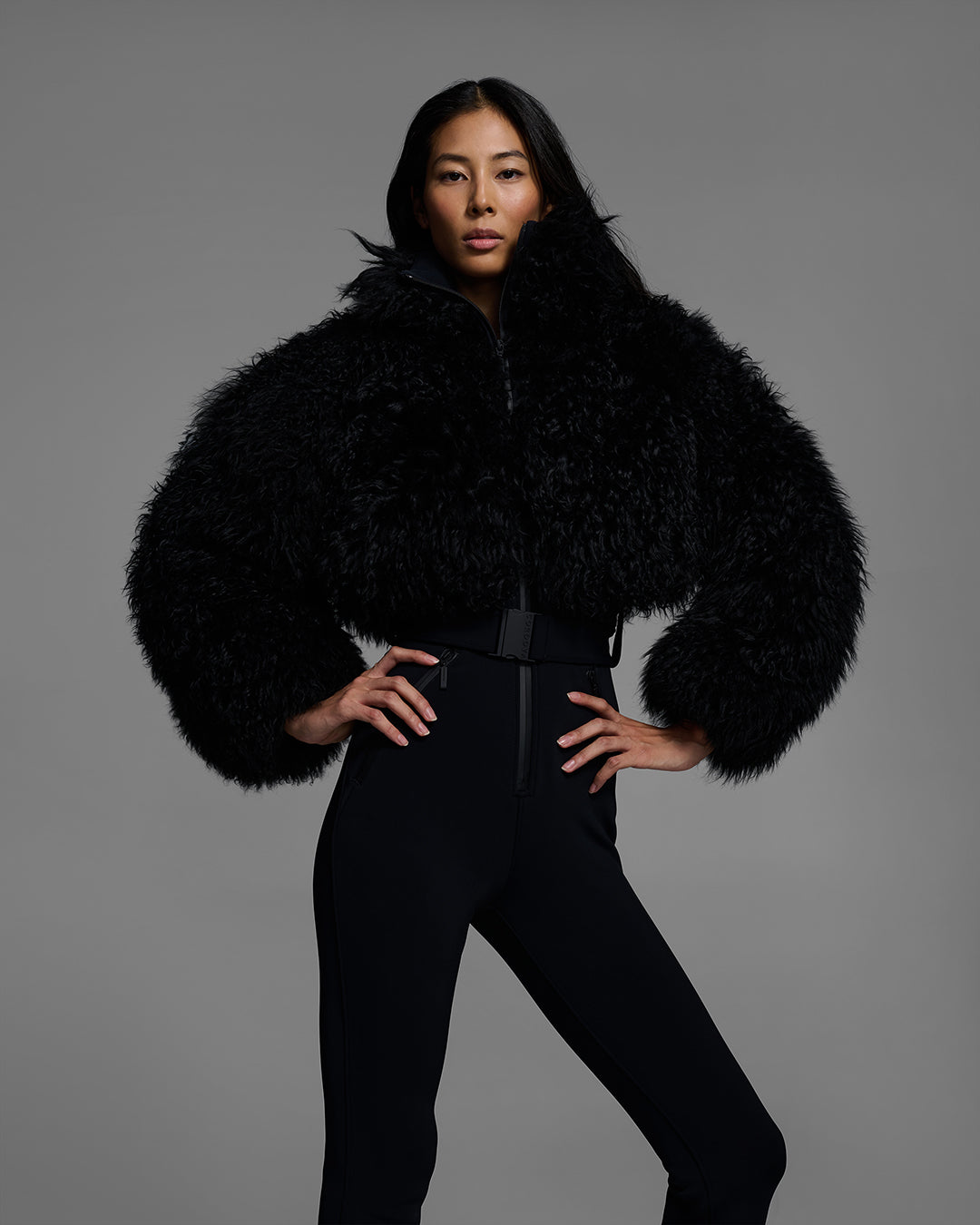 Front detail view of a woman wearing an alabaster white color ski suit with a shearling top, belted waist, and 4-way stretch pant. #color_onyx