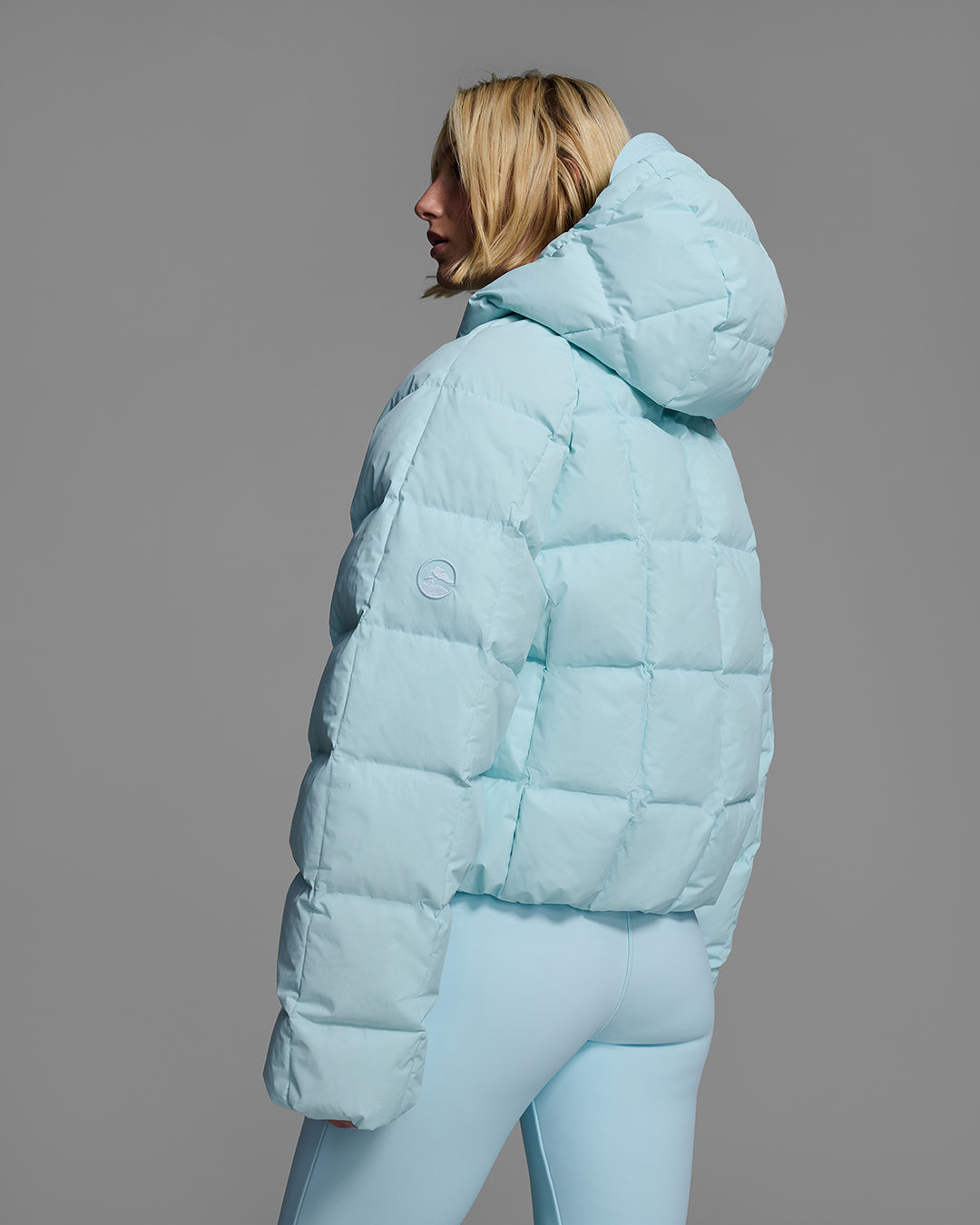 Back view of a woman wearing an iceberg blue color quilted down ski jacket with matching ski pants. #color_iceberg