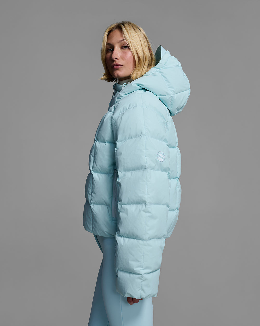 Side view of a woman wearing an iceberg blue color quilted down ski jacket with matching ski pants. #color_iceberg