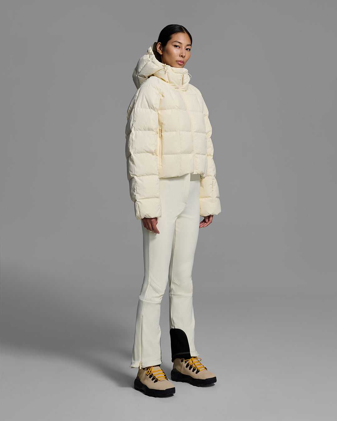 Woman wearing an off-white color quilted down ski jacket with matching ski pants. #color_alabaster