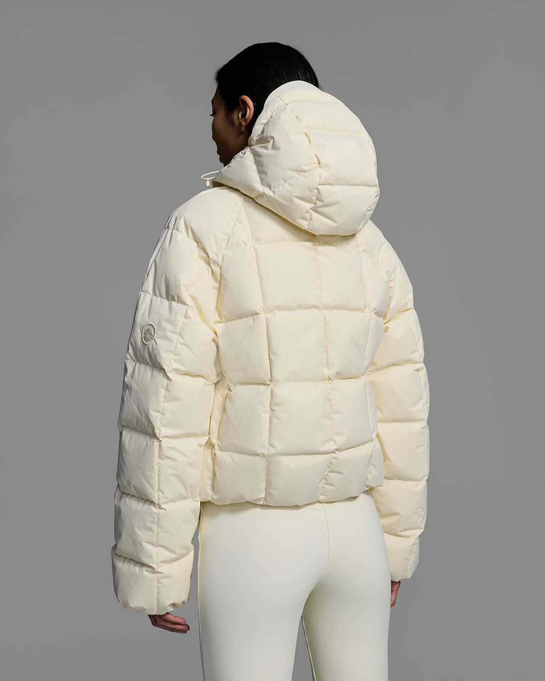 Back view of a woman wearing an off-white color quilted down ski jacket with matching ski pants. #color_alabaster