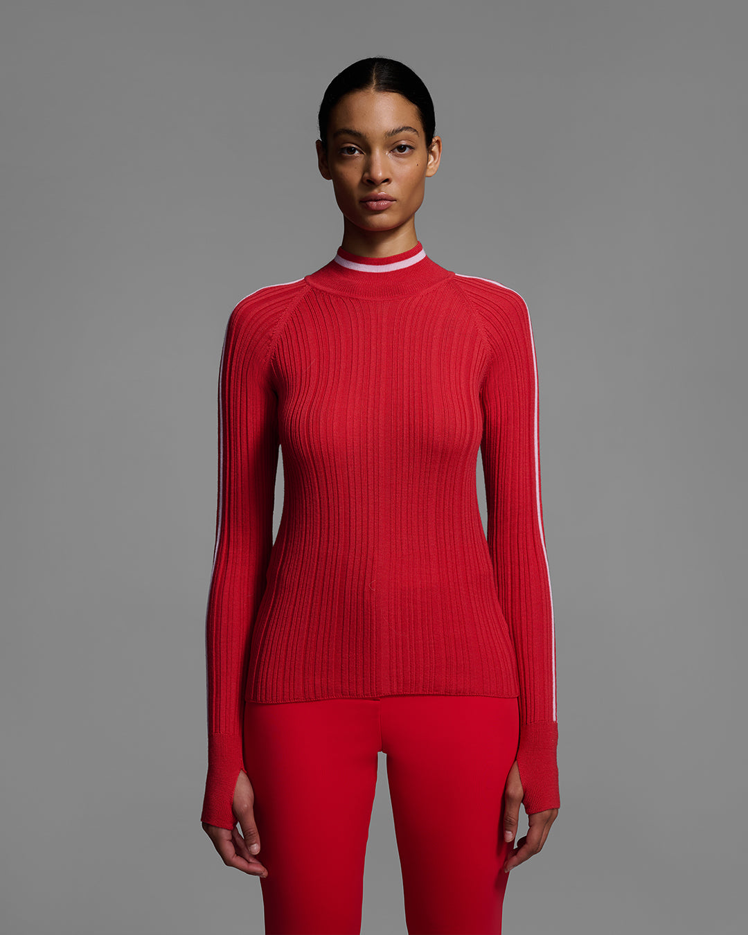 Detail view of a woman wearing a bright poppy red ski sweater with racing stripes down the sleeves and on collar, with matching red ski pants. #color_poppy
