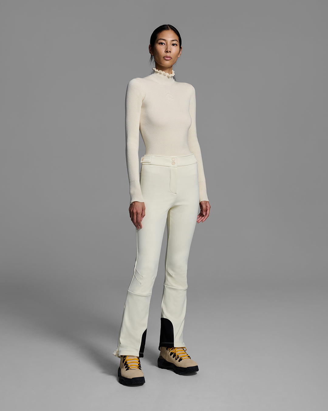 Woman wearing a 4-way stretch ski pant in alabaster white and a matching ski sweater with a ruffle neck. #color_alabaster