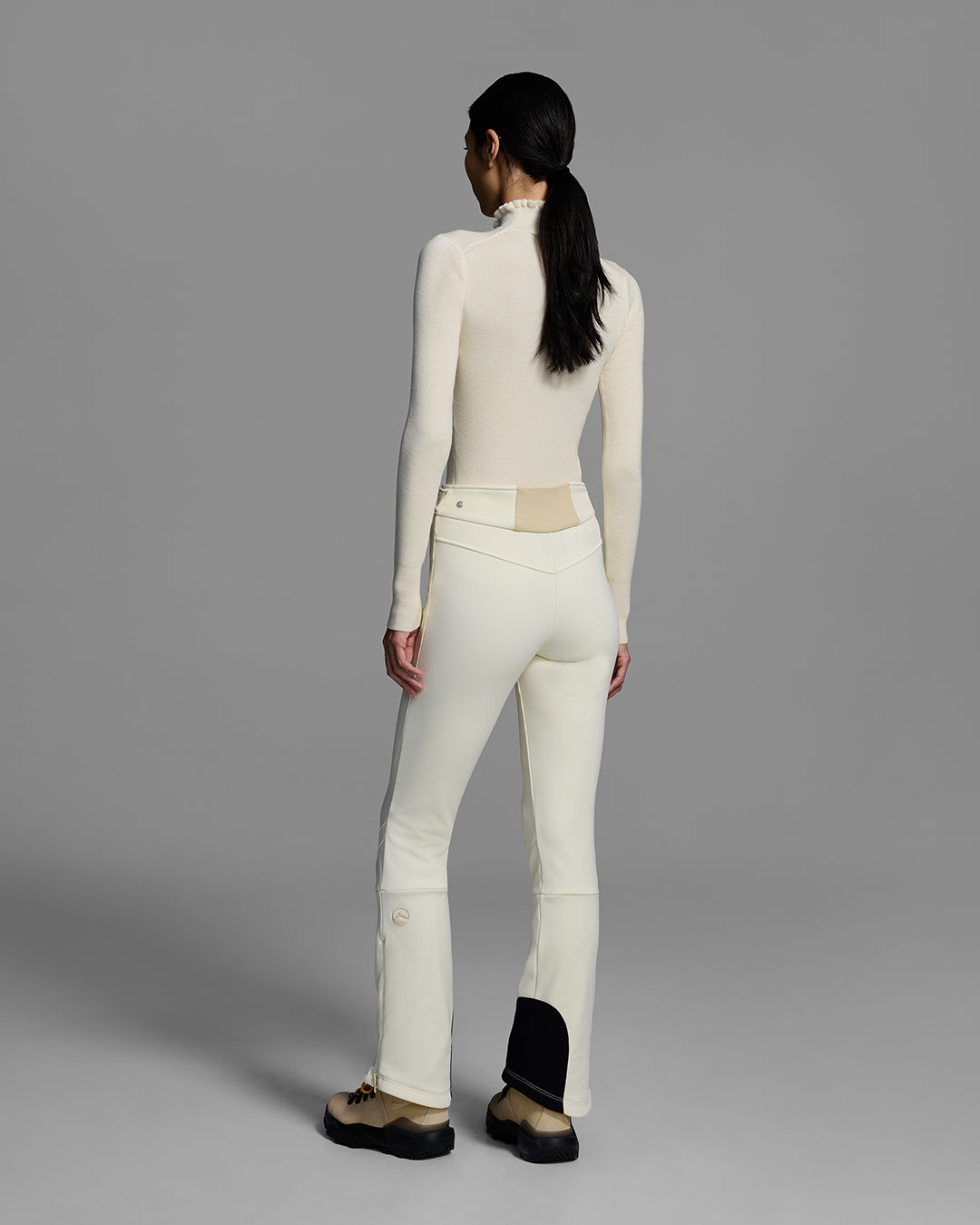 Back view of a woman wearing a 4-way stretch ski pant in alabaster white and a matching ski sweater with a ruffle neck. #color_alabaster