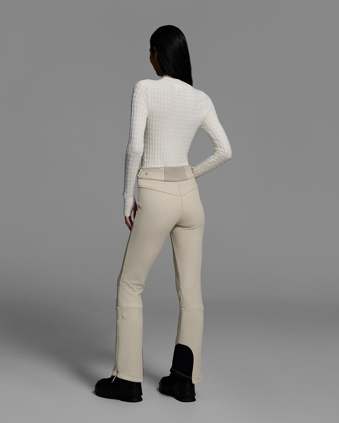 Back view of a woman wearing a 4-way stretch ski pant in birch inspired tan and a off white base layer sweater. #color_birch